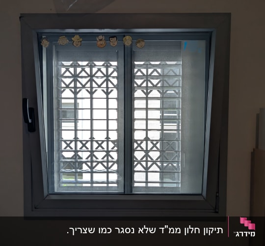 חלון עם תריסים מתכתיים ודמויות קטנות על המסגרת